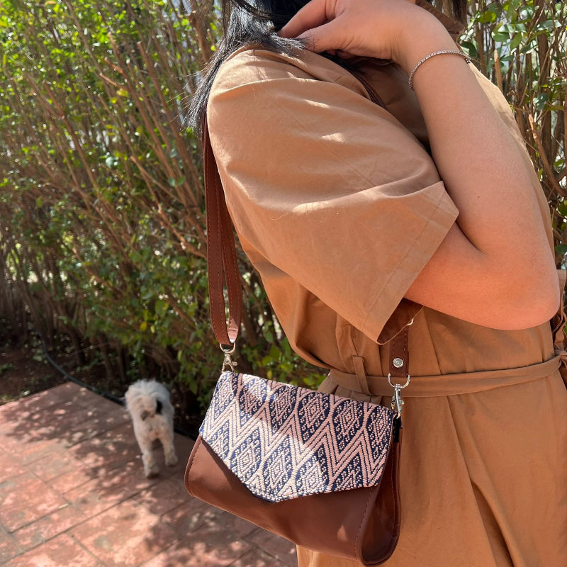 Woman wearing a brown leather crossbody bag with beige and navy geometric woven flap outdoors