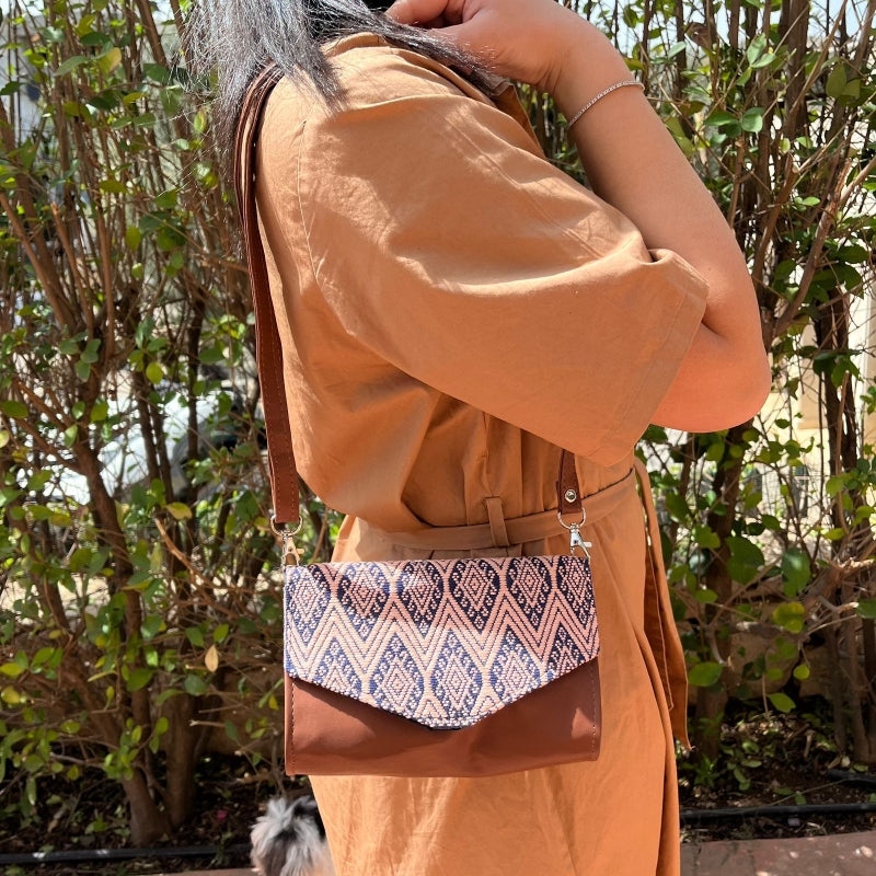 Woman wearing a brown leather crossbody bag with beige and navy geometric woven flap outdoors