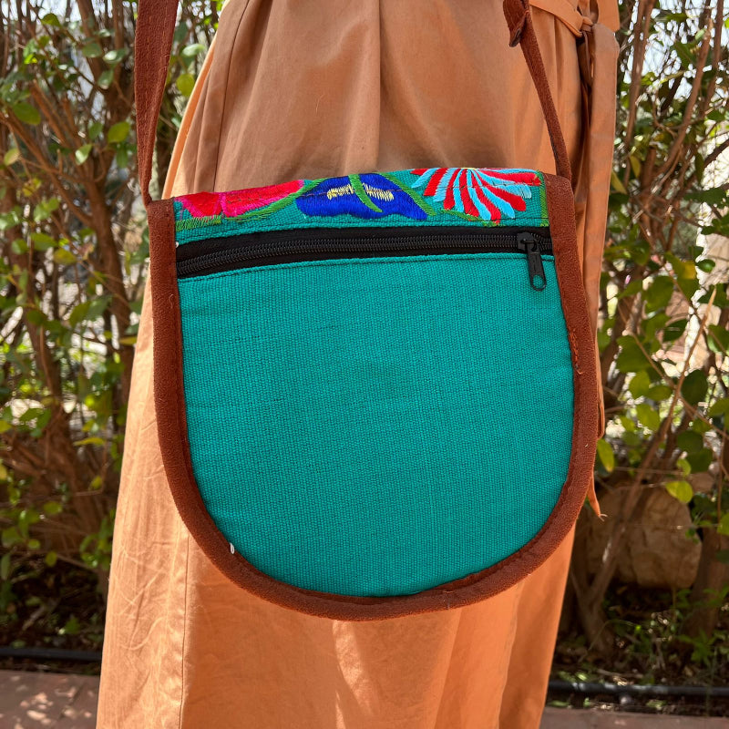 Close-up of a turquoise crossbody bag with colorful floral embroidery and tassels worn outdoors