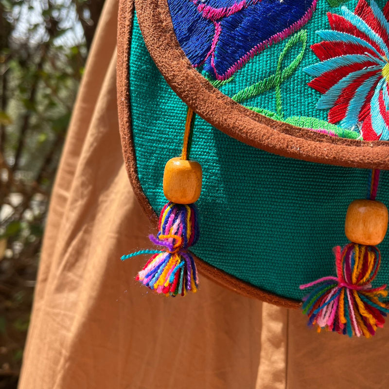 Close-up of a turquoise crossbody bag with colorful floral embroidery and tassels worn outdoors