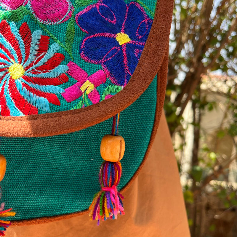 Close-up of a turquoise crossbody bag with colorful floral embroidery and tassels worn outdoors