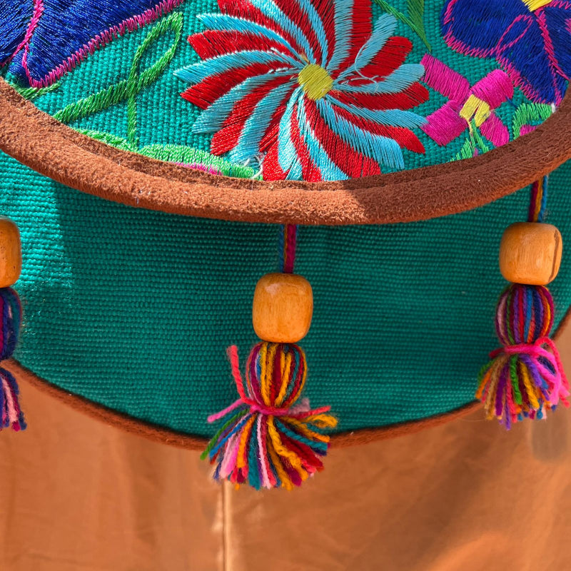 Close-up of a turquoise crossbody bag with colorful floral embroidery and tassels worn outdoors
