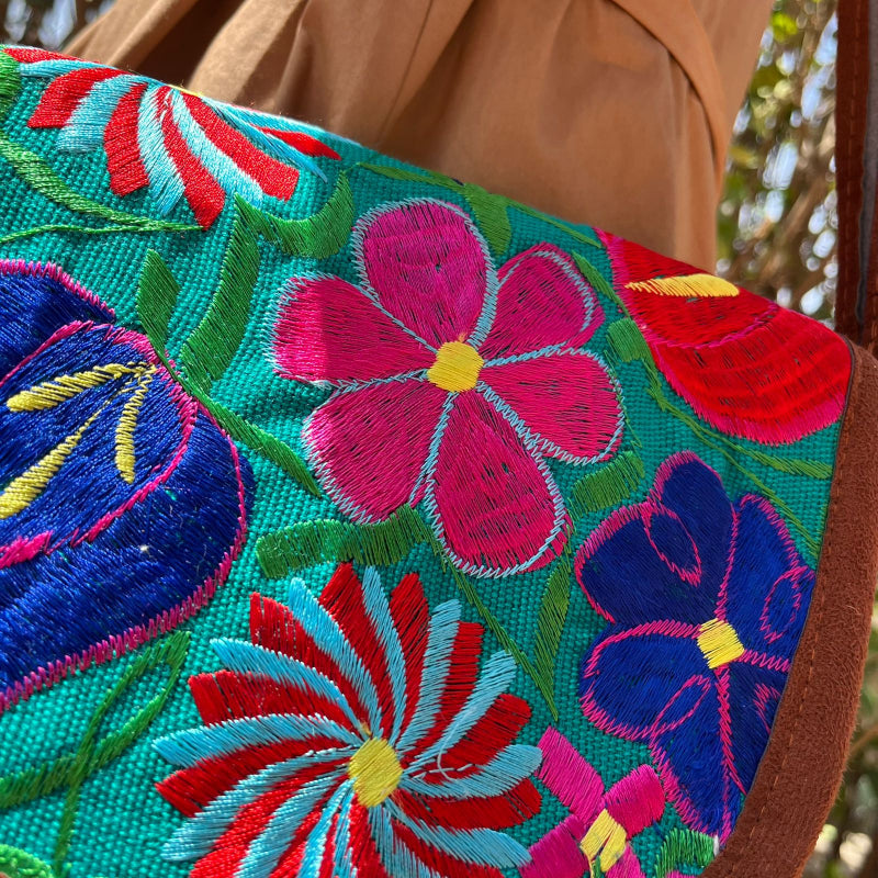 Close-up of a turquoise crossbody bag with colorful floral embroidery and tassels worn outdoors