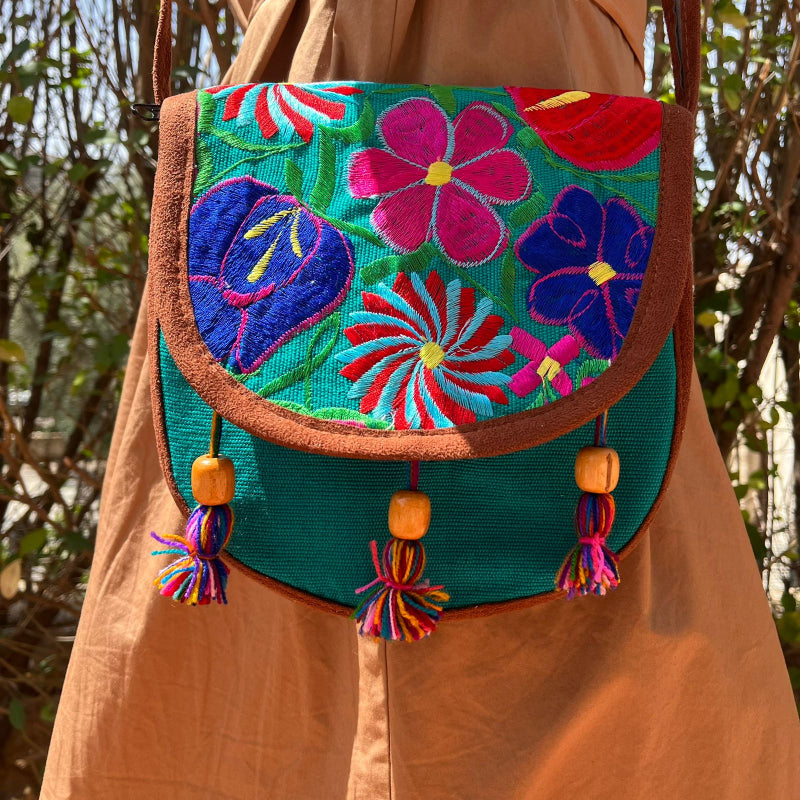 Close-up of a turquoise crossbody bag with colorful floral embroidery and tassels worn outdoors