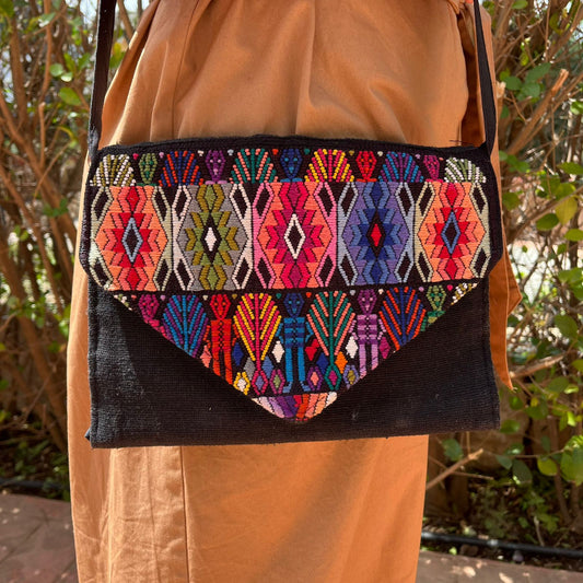 Woman wearing a black crossbody bag with vibrant multicolor geometric woven flap outdoors