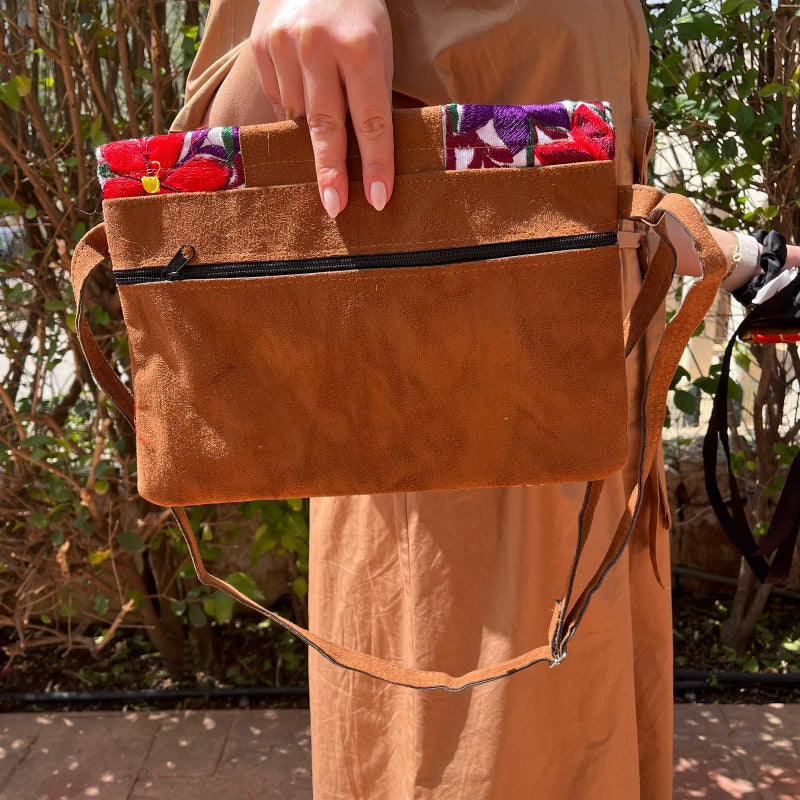 Woman wearing a floral embroidered crossbody bag with a brown leather panel and tassel detail outdoors