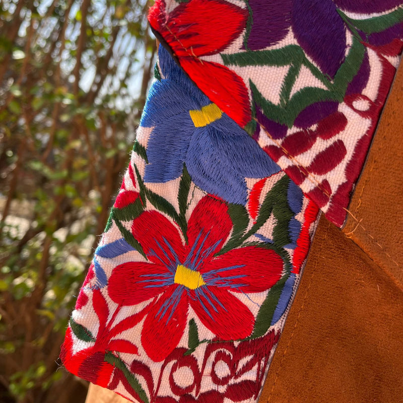 Woman wearing a floral embroidered crossbody bag with a brown leather panel and tassel detail outdoors