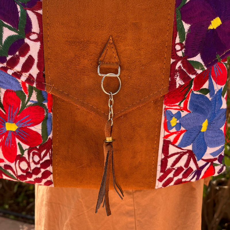 Woman wearing a floral embroidered crossbody bag with a brown leather panel and tassel detail outdoors