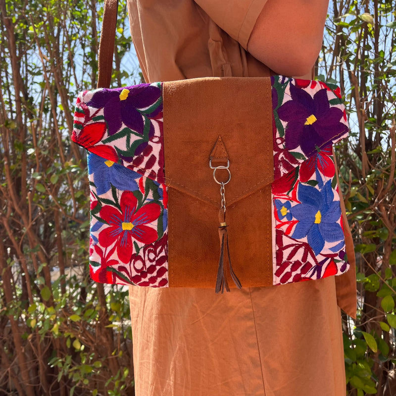 Woman wearing a floral embroidered crossbody bag with a brown leather panel and tassel detail outdoors