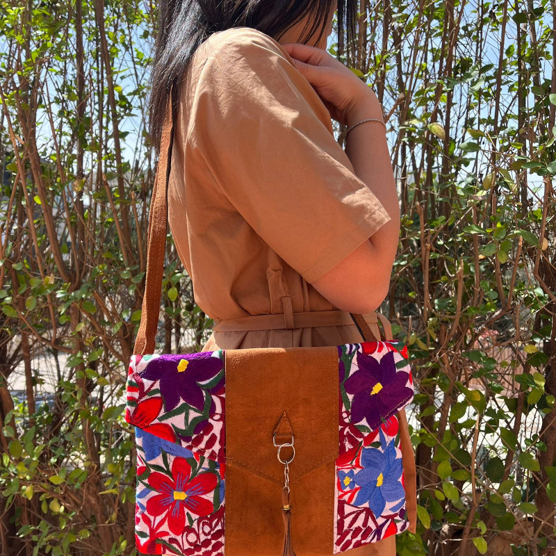 Woman wearing a floral embroidered crossbody bag with a brown leather panel and tassel detail outdoors