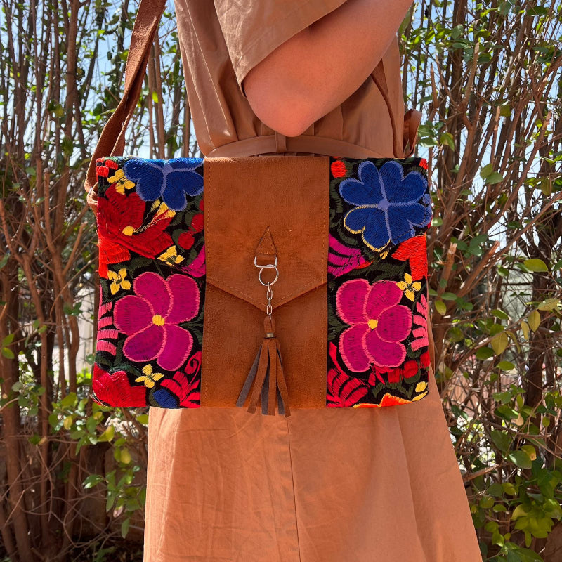 Woman wearing a black floral embroidered crossbody bag with a brown leather panel and tassel detail outdoors