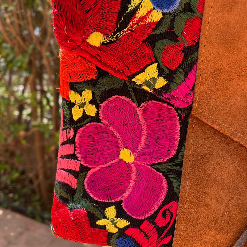 Woman wearing a black floral embroidered crossbody bag with a brown leather panel and tassel detail outdoors
