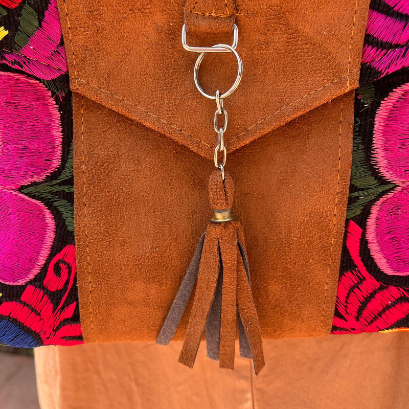 Woman wearing a black floral embroidered crossbody bag with a brown leather panel and tassel detail outdoors