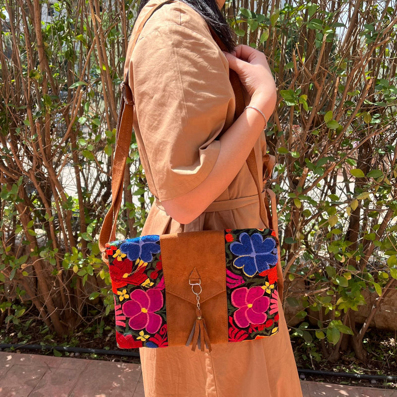 Woman wearing a black floral embroidered crossbody bag with a brown leather panel and tassel detail outdoors