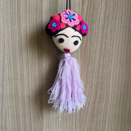 Handmade Frida Kahlo felt ornament with pink floral embroidery and soft pastel tassel hanging on wooden background