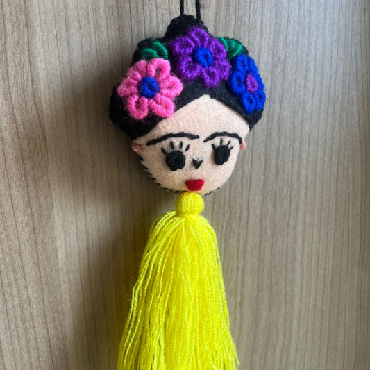 Handmade Frida Kahlo felt ornament with multicolor floral embroidery and bright yellow tassel hanging on wooden background