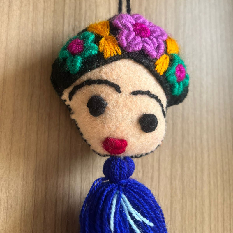 Handmade Frida Kahlo felt ornament with multicolor floral embroidery and blue tassel hanging on wooden background