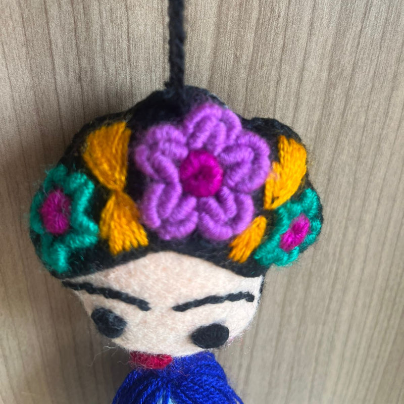 Handmade Frida Kahlo felt ornament with multicolor floral embroidery and blue tassel hanging on wooden background