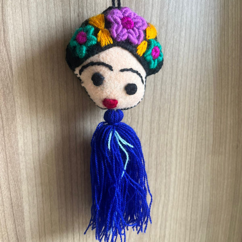 Handmade Frida Kahlo felt ornament with multicolor floral embroidery and blue tassel hanging on wooden background