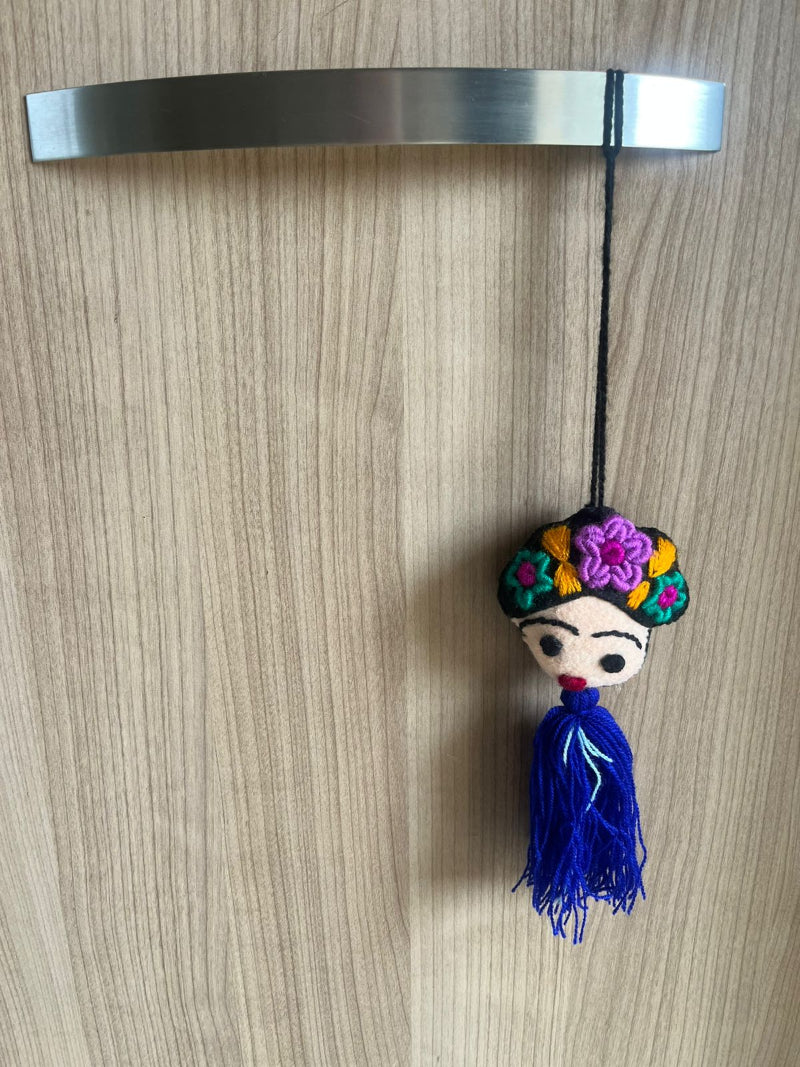 Handmade Frida Kahlo felt ornament with multicolor floral embroidery and blue tassel hanging on wooden background