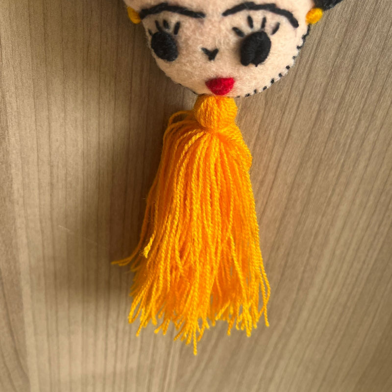 Handmade Frida Kahlo felt ornament with multicolor floral embroidery and bright orange tassel hanging on wooden background