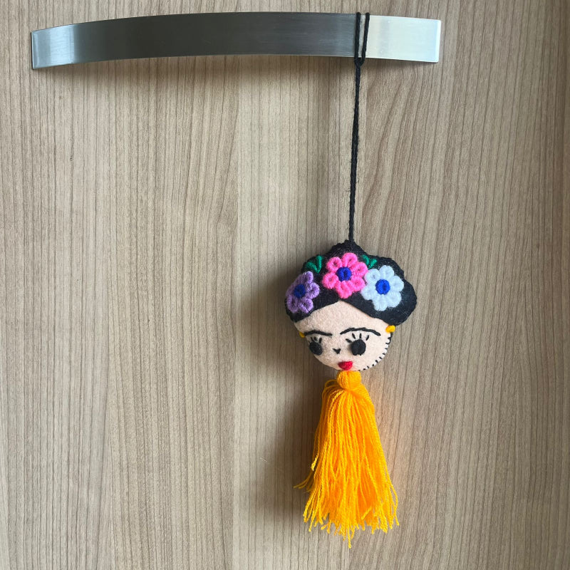 Handmade Frida Kahlo felt ornament with multicolor floral embroidery and bright orange tassel hanging on wooden background