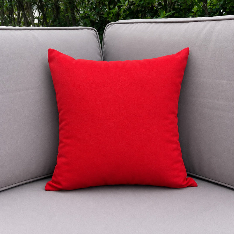 Red pillow on a gray outdoor sofa with greenery in the background