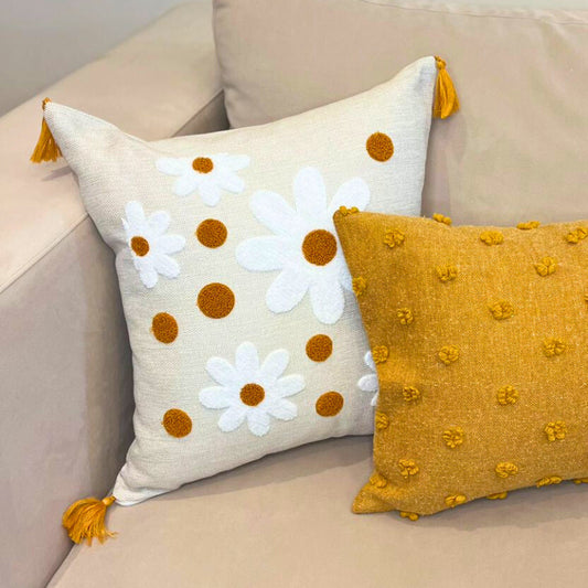 Square embroidered daisy cushion cover with mustard accents and tassels on beige sofa