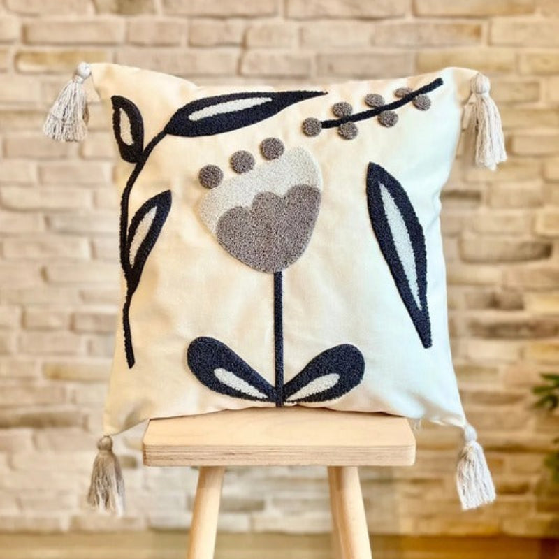 Embroidered floral cushion with navy and grey design, soft cream fabric, and tassel accents on each corner, perfect for home decor."
