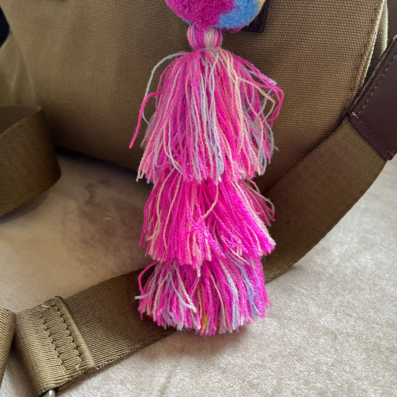 Colorful pom pom tassel bag charm with pink and pastel yarn attached to a beige handbag