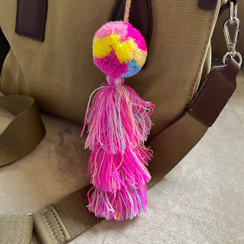 Colorful pom pom tassel bag charm with pink and pastel yarn attached to a beige handbag