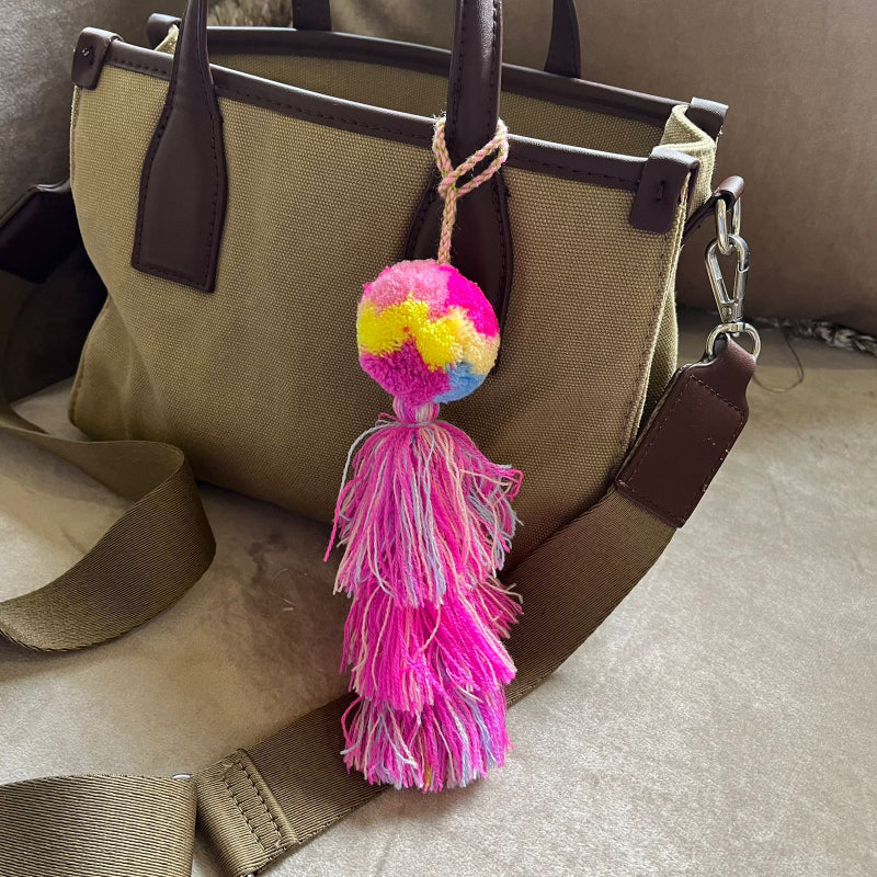 Colorful pom pom tassel bag charm with pink and pastel yarn attached to a beige handbag