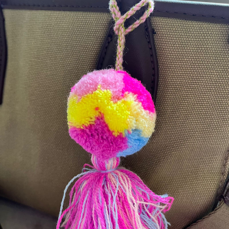 Colorful pom pom tassel bag charm with pink and pastel yarn attached to a beige handbag