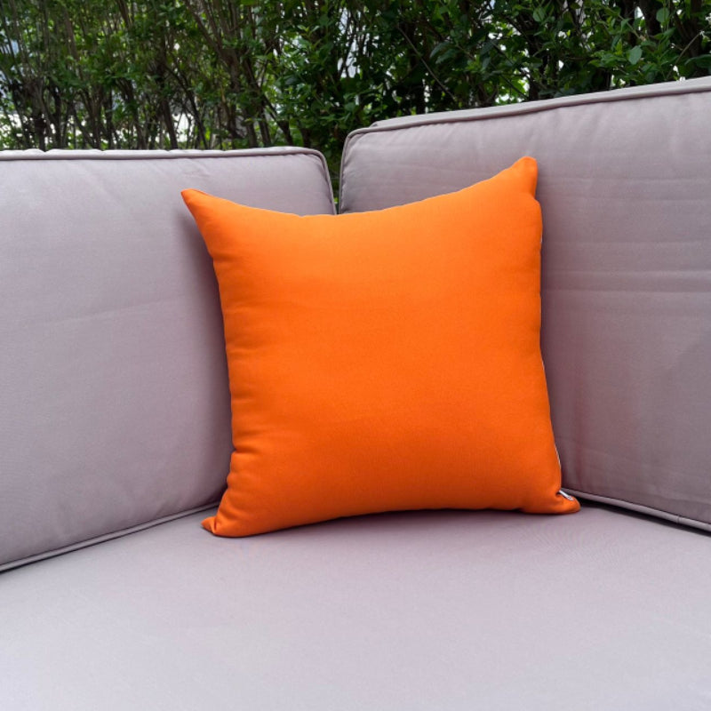 Orange pillow on a gray outdoor sofa with greenery in the background