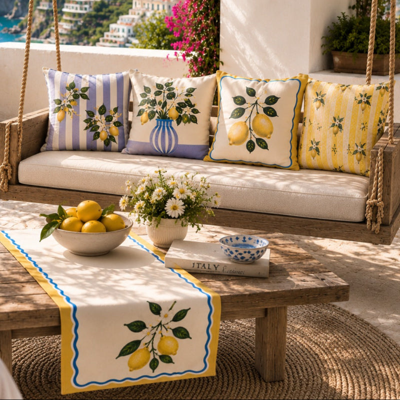 Set of four Mediterranean-inspired decorative cushion covers featuring lemons, citrus blossoms, elegant striped patterns, and a lavender ceramic vase displayed on a modern cream sofa.