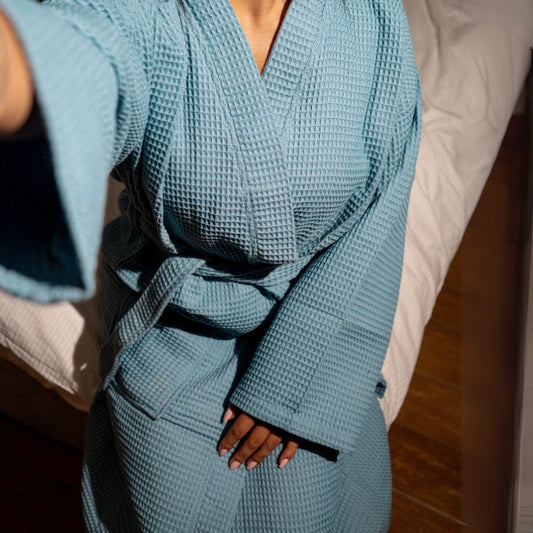 Blue waffle cotton bathrobe with belt and front pockets worn by woman on a balcony