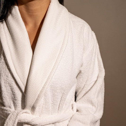 Unisex cotton terry bathrobe with shawl collar and waist belt, worn by woman near window in natural light