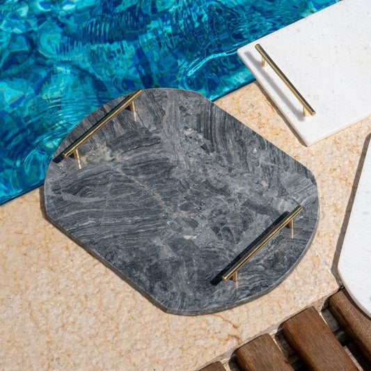 dark grey oval capsule-shaped marble tray with brass handles placed by the pool