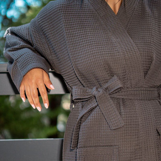 Grey waffle cotton bathrobe with belt and front pockets worn by woman on a balcony