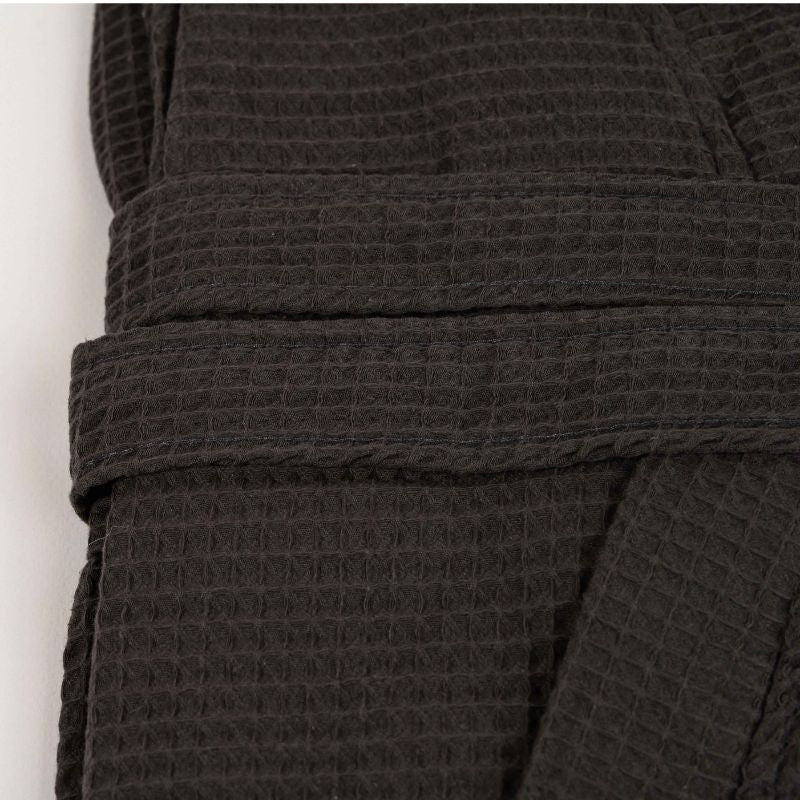 Grey waffle cotton bathrobe with belt and front pockets worn by woman on a balcony