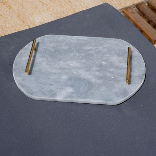 Light grey oval capsule-shaped marble tray with brass handles placed by the pool