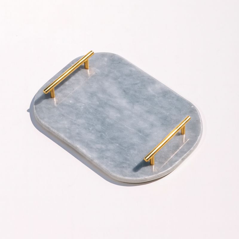Light grey oval capsule-shaped marble tray with brass handles placed by the pool