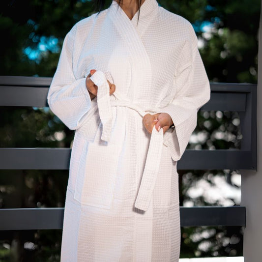 White waffle cotton bathrobe with belt and front pockets worn by woman on a balcony