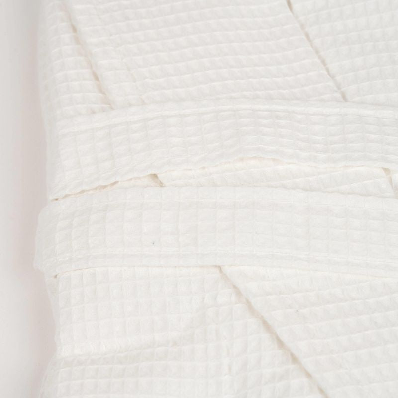 White waffle cotton bathrobe with belt and front pockets worn by woman on a balcony
